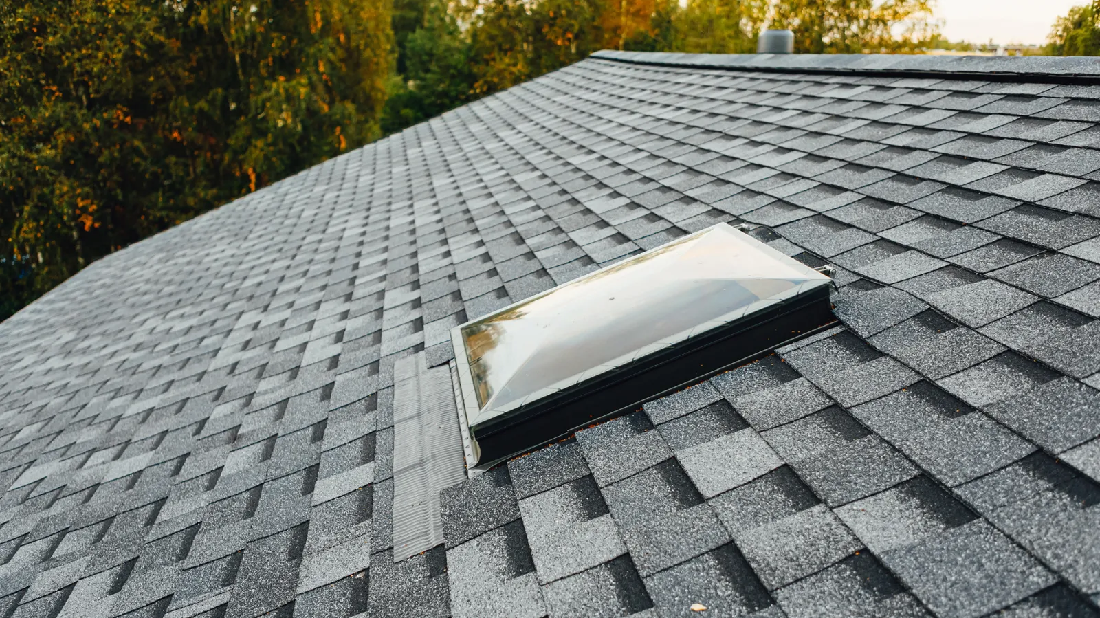 A domed skylight mounted on a dark gray asphalt shingle roof